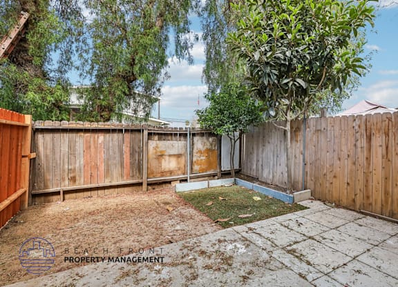 A backyard with a wooden fence and a tree.