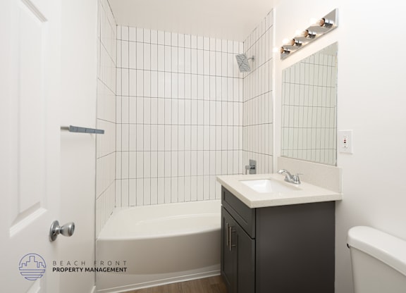 A white tiled bathroom with a sink, bathtub, and toilet.