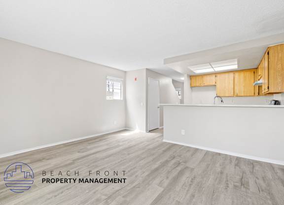 A spacious room with wooden flooring and a logo for Beach Front Property Management.