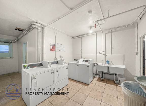 A clean, empty room with a washing machine and a dryer, with the logo of Beach Front Property Management in the corner.