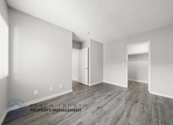 A room with wooden flooring and white walls, with a logo for Beach Front Property Management in the bottom left corner.
