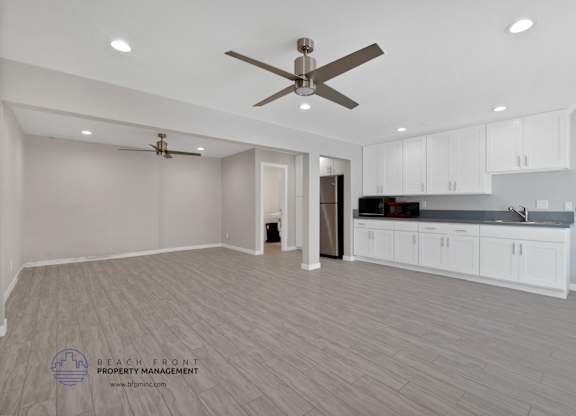 A spacious kitchen and living room with a ceiling fan and lighting fixtures.