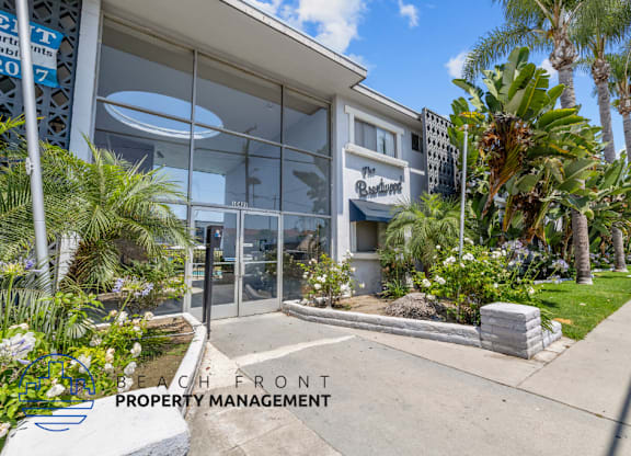 the front of a building with palm trees and a sidewalk