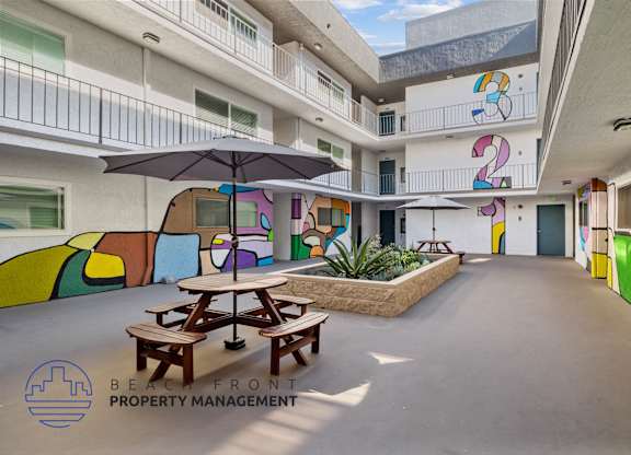 A colorful mural on the side of a building with a picnic table and umbrella in front.