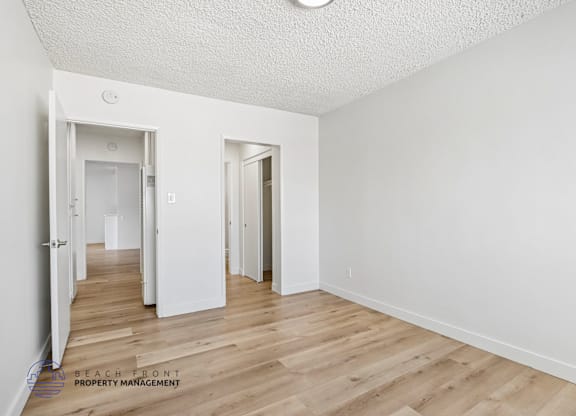 A room with white walls and wooden flooring, with two doors visible.