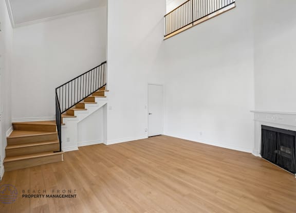 A spacious room with a fireplace and a staircase with a black railing.