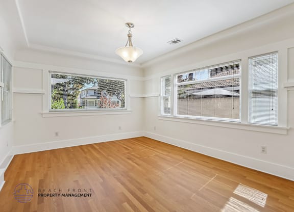A room with wooden floors and white walls, with a window showing a view of a house.