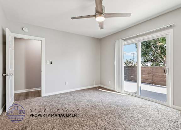 A spacious room with a ceiling fan and sliding glass doors leading to a backyard.