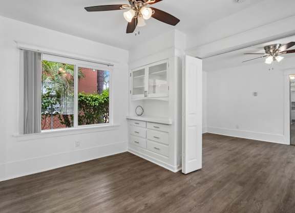 A room with a ceiling fan and a window with a view of a red building.
