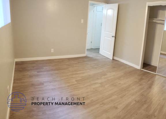 A spacious room with wooden flooring and a sliding glass door leading to a balcony.