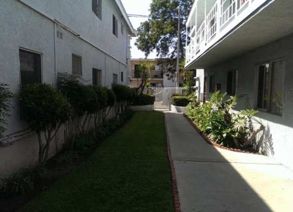 A long, narrow walkway between two buildings with green grass on either side.