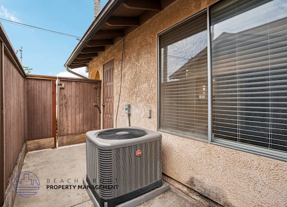 An air conditioning unit is placed on a concrete slab outside a house.