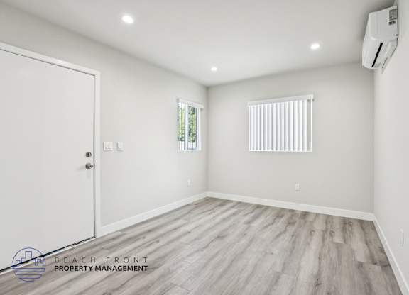 A room with a white door, window with blinds, and a wooden floor.