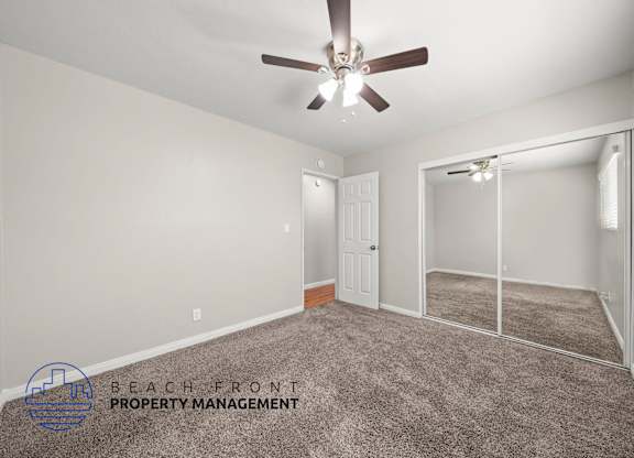 A spacious room with a ceiling fan and a sliding glass door leading to a balcony.