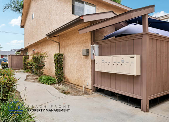 A wooden utility box is attached to a tan house.