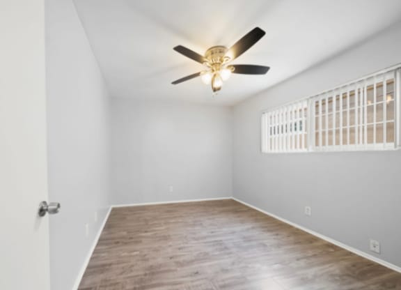 A room with a ceiling fan and a window with bars.