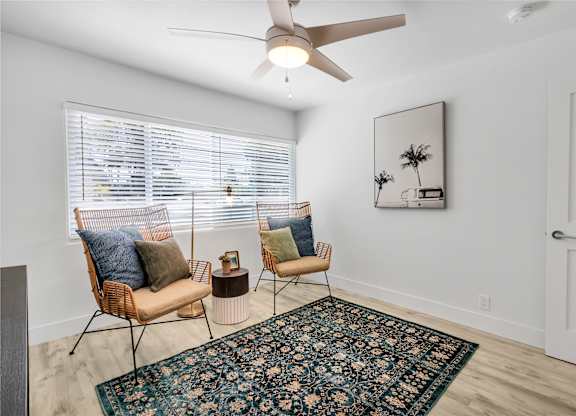 A room with a rug, two chairs and a ceiling fan.