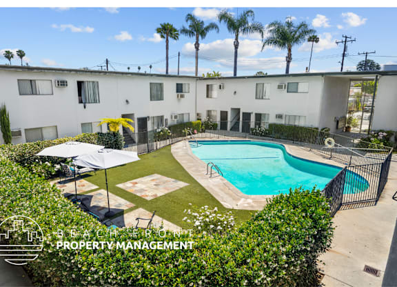 an aerial view of a pool in front of a white building with palm trees