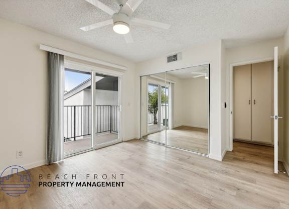 A spacious room with a sliding glass door leading to a balcony, a ceiling fan, and a logo for Beach Front Property Management.