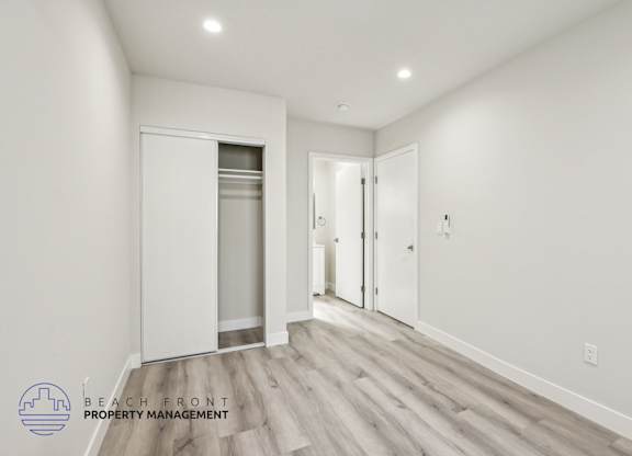 A spacious room with wooden flooring and white walls, featuring a white door and a white closet with a glass window.