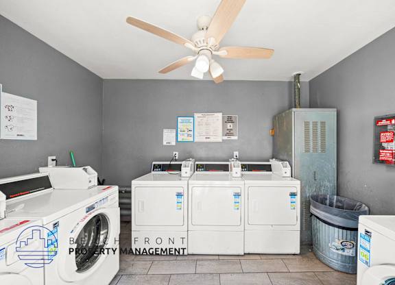 A laundry room with a washer and dryer, a fan, and a trash can.