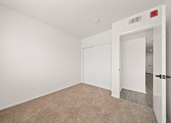 a bedroom with white walls and carpet and a door to a closet