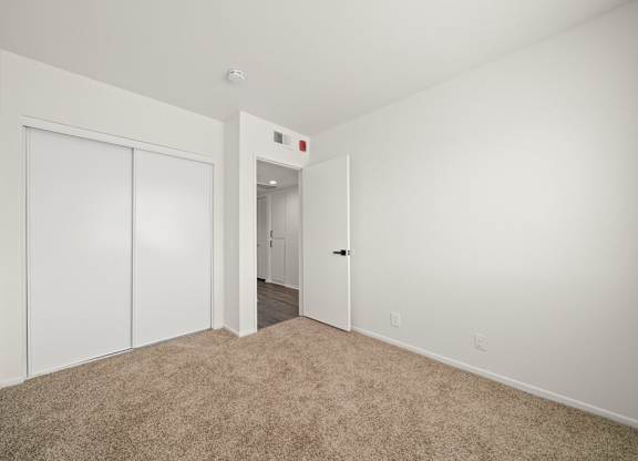 a bedroom with white walls and carpet and a door to a hallway
