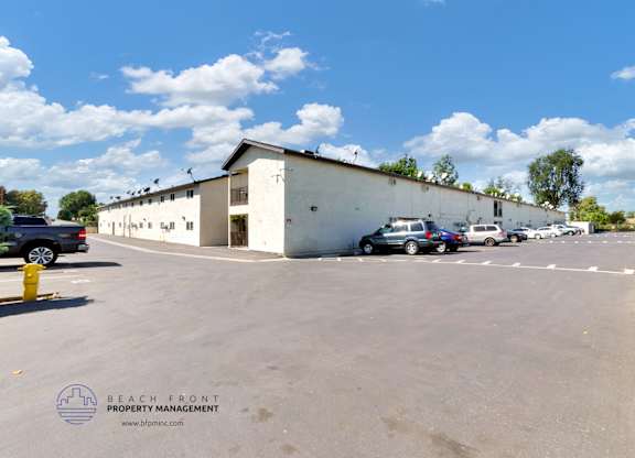 A parking lot with a white building and cars parked in front.
