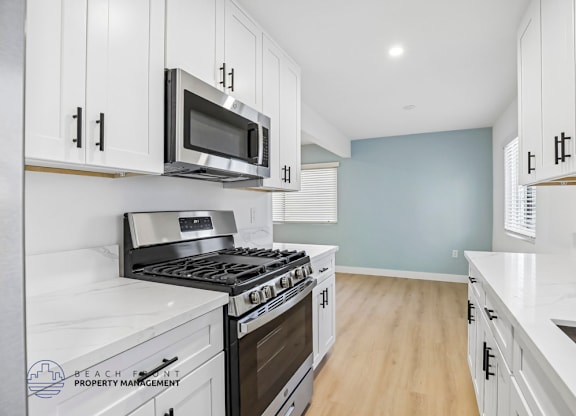 A kitchen with white cabinets and a stainless steel stove top oven.