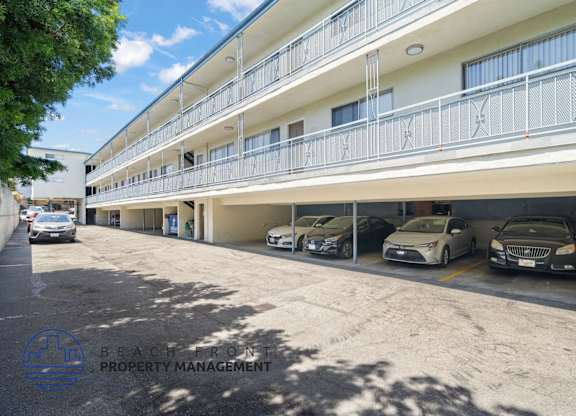 A parking lot with cars parked in front of a building with a balcony.