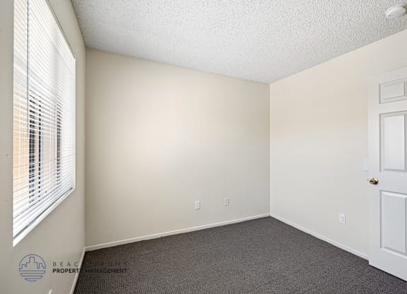 A room with a white door, carpeted floor, and a window with blinds.