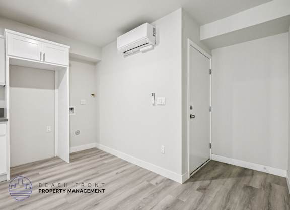 A white room with a wooden floor and a wall-mounted air conditioner unit.