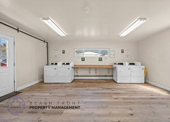 A room with a wooden floor and white walls has a row of printers on a table.