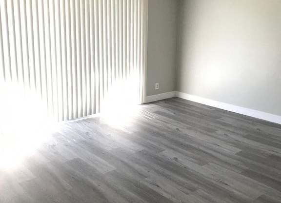 A room with wooden flooring and a window with blinds.