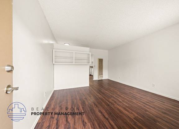 A room with wooden floors and white walls, with a logo for Beach Front Property Management in the bottom left corner.