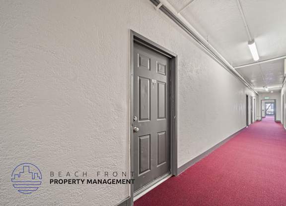 A long hallway with a red carpet and a door on the left side.