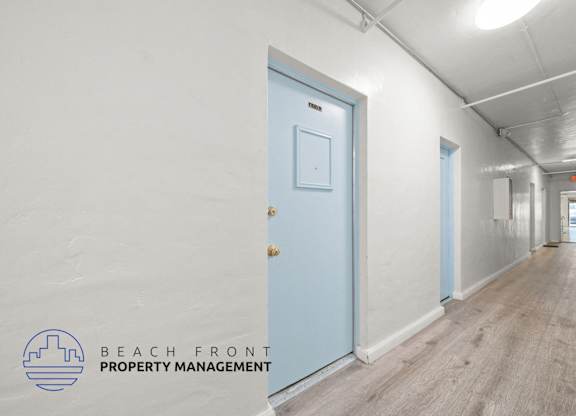 A hallway with a blue door and a logo for Beach Front Property Management.