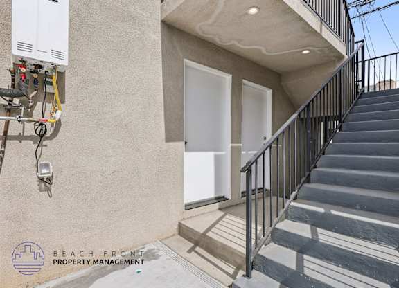 A staircase with a metal railing leads to a white door on a tan building.