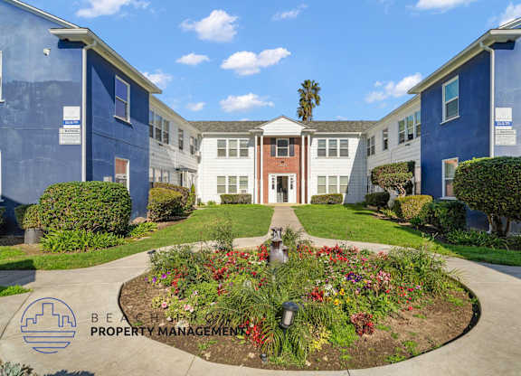 A garden in front of a building with the logo of Beachfront Property Management.