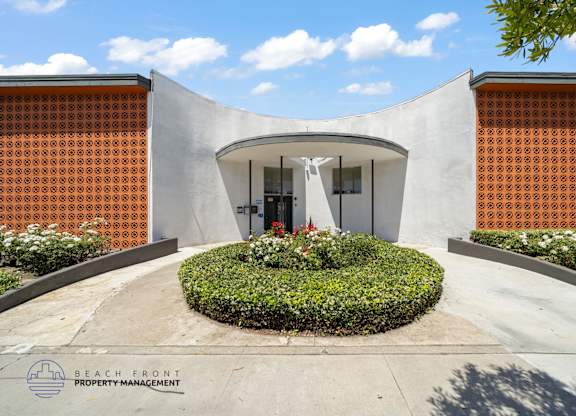 A modern building entrance with a circular flower bed in front.