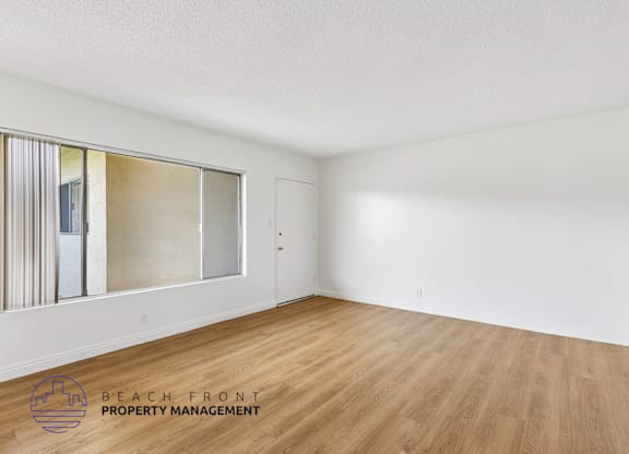 A room with wooden flooring and a large window with a view of the beach.