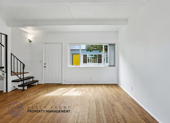 A spacious room with wooden floors and white walls, featuring a staircase with black railings.