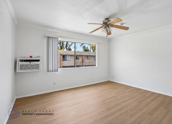 A room with a ceiling fan and a window overlooking a beachfront property.
