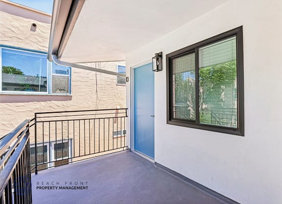 A balcony with a blue door and a window overlooking a beach.