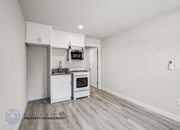 A kitchen with white cabinets and appliances in a room with wooden flooring.