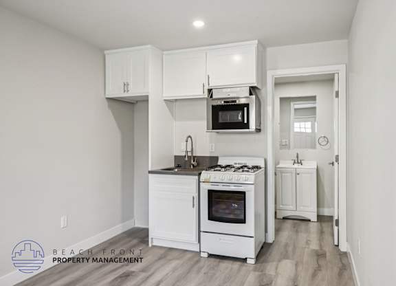 A kitchen with white cabinets and appliances, a microwave above the stove, and a doorway leading to another room.