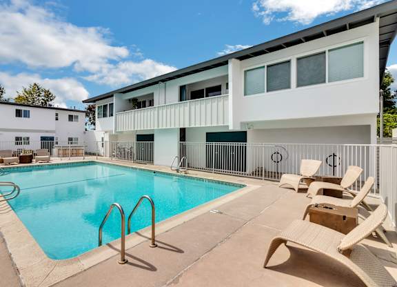 A swimming pool surrounded by chairs and a white building in the background.