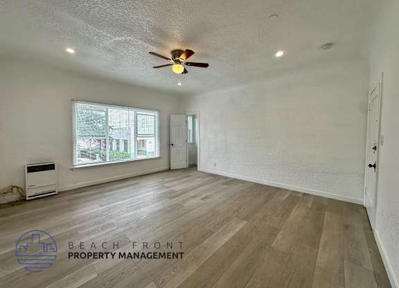 A spacious room with wooden flooring and a ceiling fan.