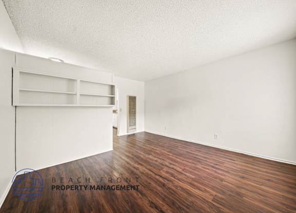 A room with wooden floors and white walls, with a shelving unit and a door.