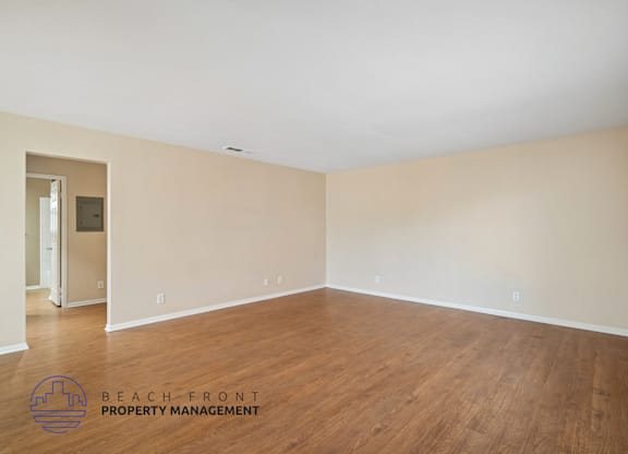 A spacious room with wooden flooring and a logo for Beach Front Property Management in the corner.